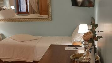 Hotelkamer met een bed, een bureau met stoel, een aan de muur bevestigde televisie en een spiegel boven het bed.