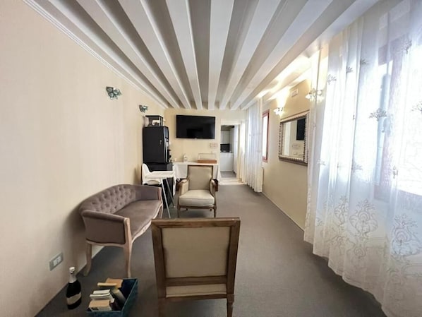 Ein Hotelzimmer mit einer Couch, Sesseln, einem Fernseher, einem kleinen Tisch und einem Fenster mit Vorhängen.