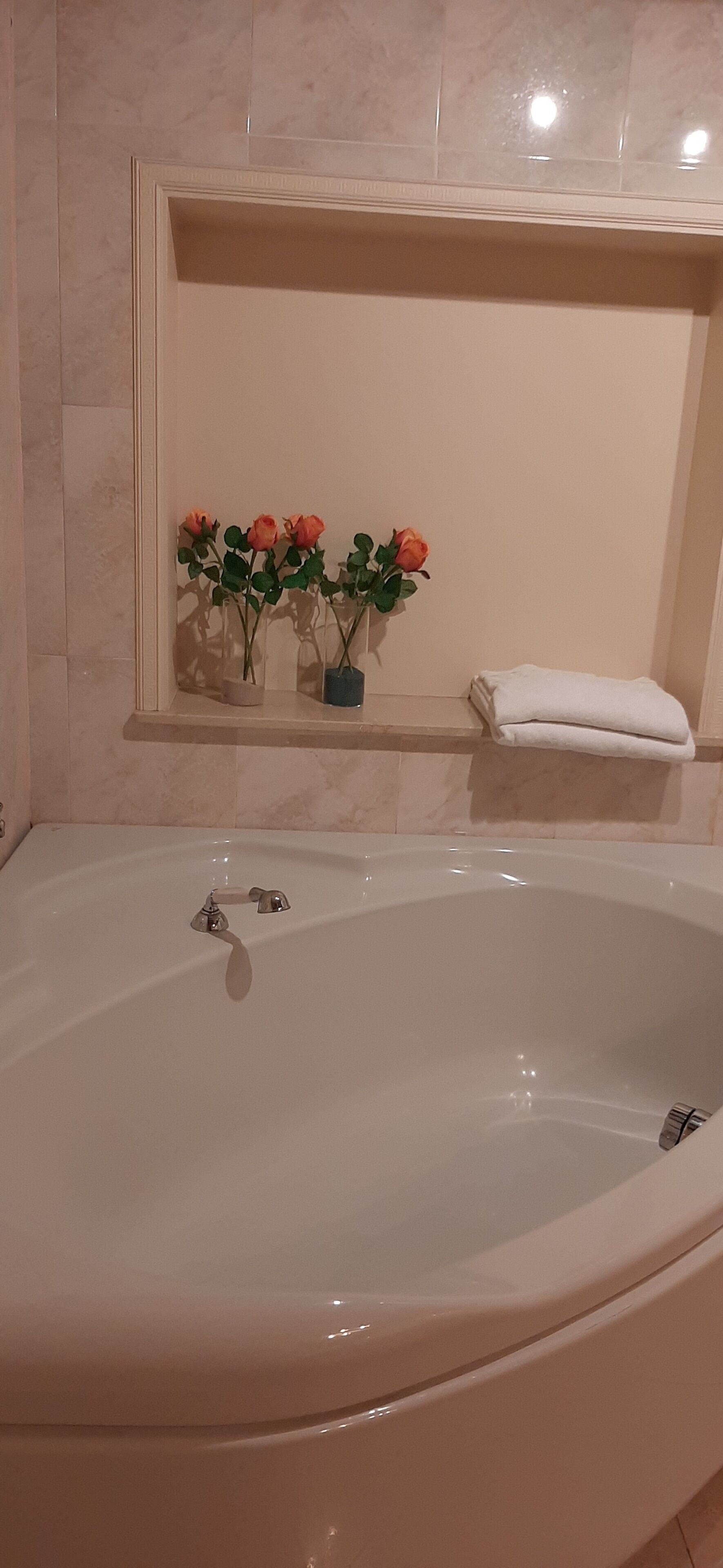 Un bagno con una vasca da bagno grande, un porta asciugamani e tre rose in vaso su uno scaffale.