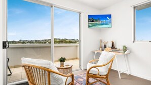 A balcony with a view of a coastal landscape, a desk with a chair, and a television mounted on the wall.