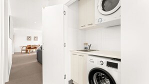 A compact, modern kitchen with a built-in washing machine, a sink, and a dining area with a table and chairs.