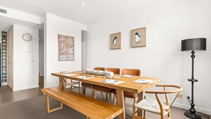 A dining area with a wooden table, benches, and chairs. There are framed artworks on the wall, a clock, and a floor lamp.
