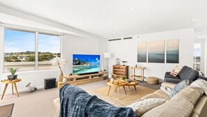 A modern living room with a large TV, comfortable seating, a wooden coffee table, and artwork on the walls.