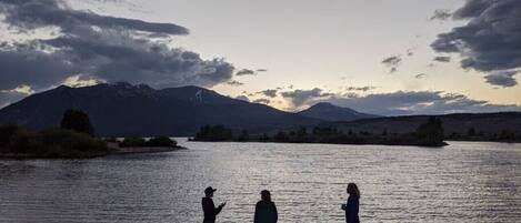 Three people standing by a lake with mountains in the background.