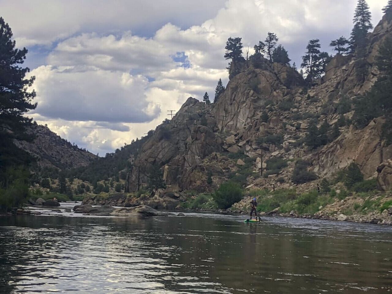 Un río con una persona remando, rodeado de acantilados rocosos y árboles.
