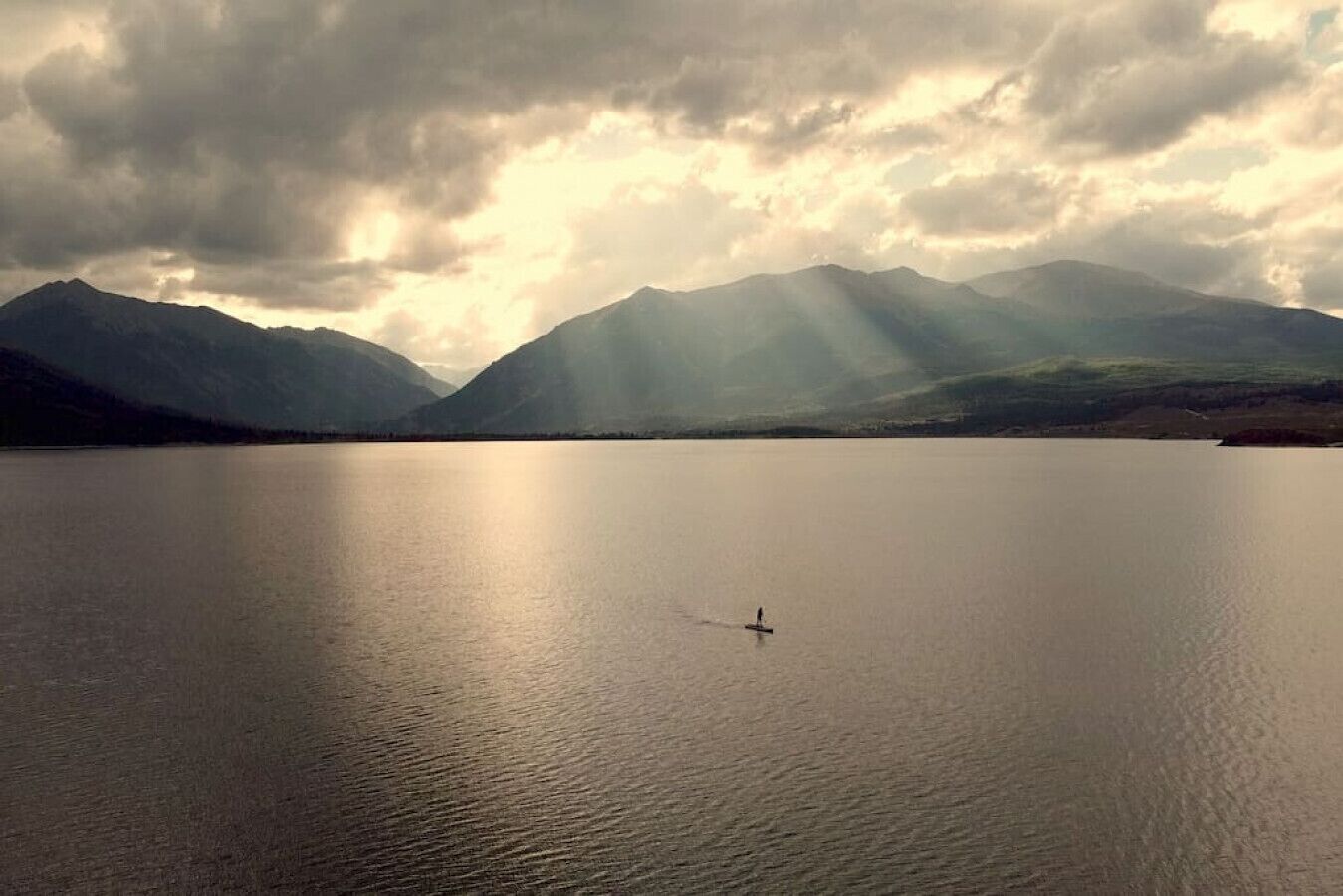 Un lac paisible, avec des montagnes en arrière-plan et un seul bateau sur l’eau.