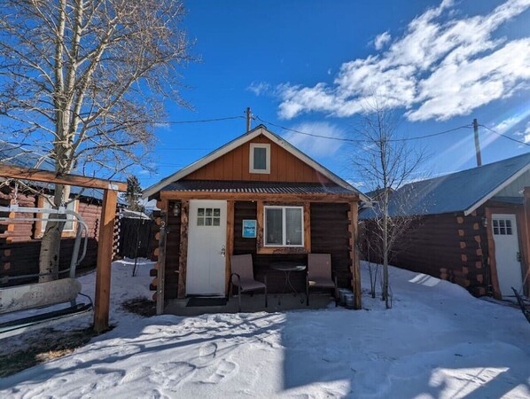 A wooden cabin with a front porch, a small table, and two chairs.