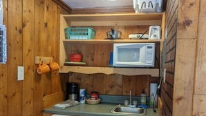 A compact kitchen with wooden walls, a built-in microwave, a small refrigerator, and a trash bin. - Stay Twin Lakes Cabin 4 (Twin Lakes)