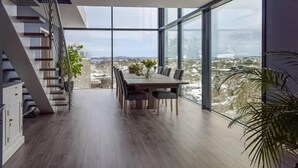 Ett modernt matområde med ett stort bord och stolar, en trappa och utsikt över ett snötäckt landskap genom stora fönster.