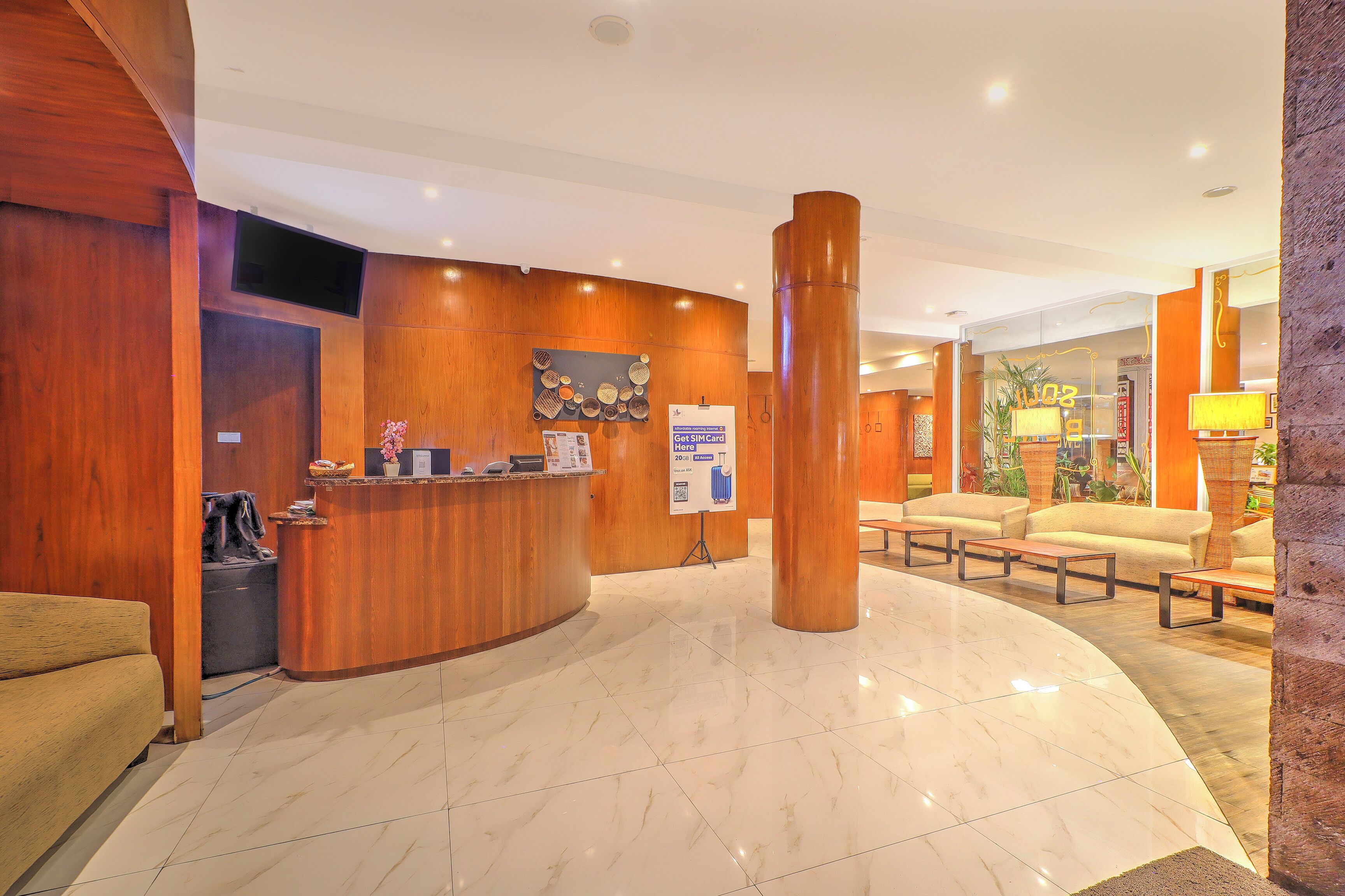 A hotel reception area with a wooden reception desk, a seating area with sofas, and a large pillar.