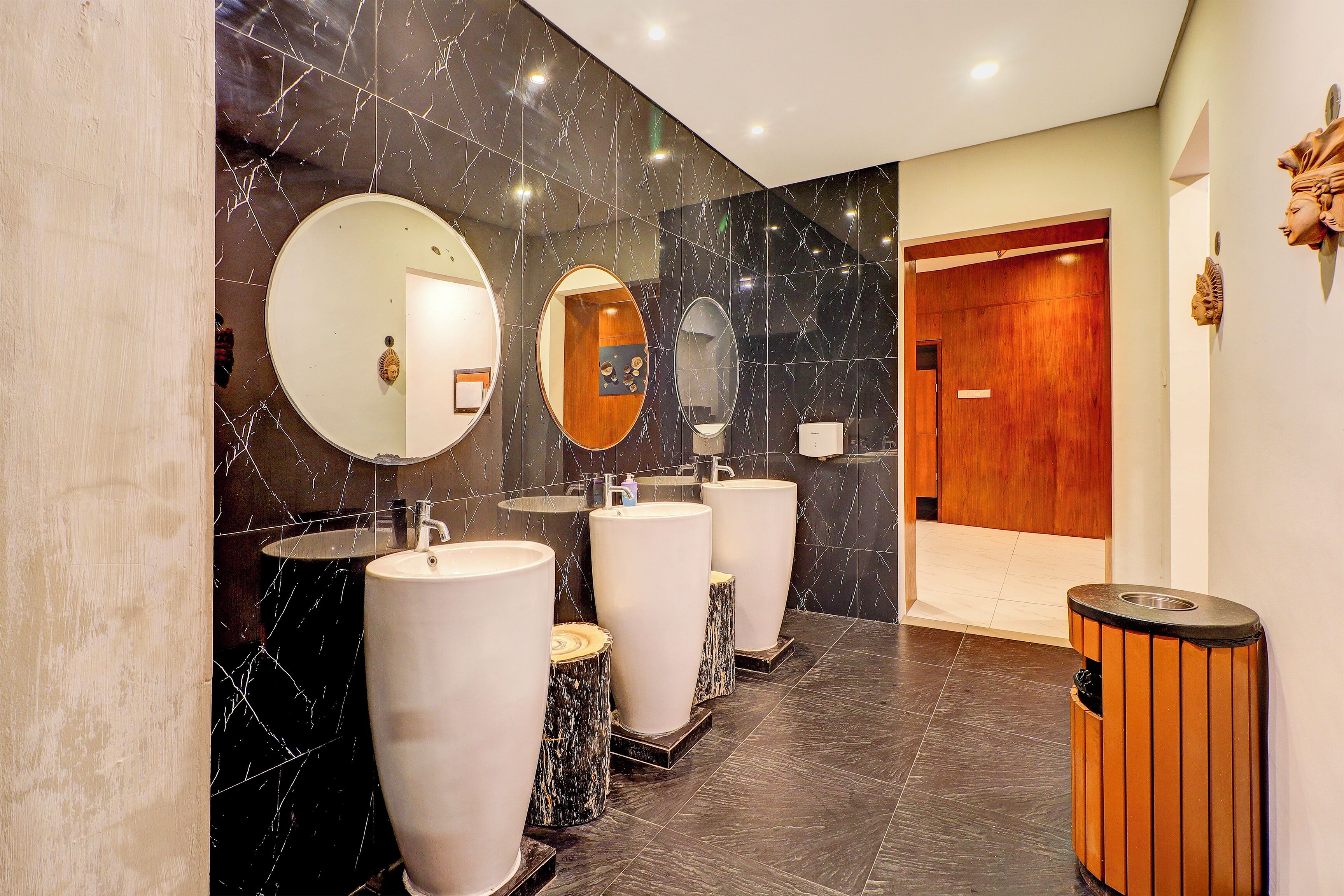 Un baño moderno con tres lavamanos, paredes de mármol y una puerta de madera.