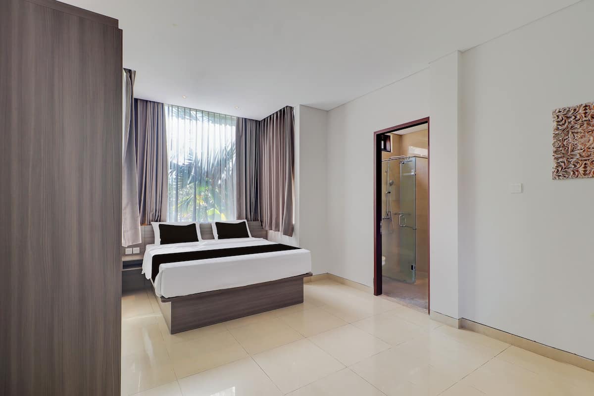 Une chambre d’hôtel moderne dotée d’un grand lit, d’un dressing et d’une salle de bain avec une douche en verre.
