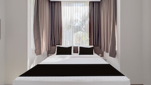 Habitación de hotel moderna con una cama grande, cortinas de gasa y vistas a zonas verdes.