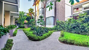 Un edificio moderno con un sendero que conduce a una entrada con puerta, rodeado de exuberante follaje y palmeras.