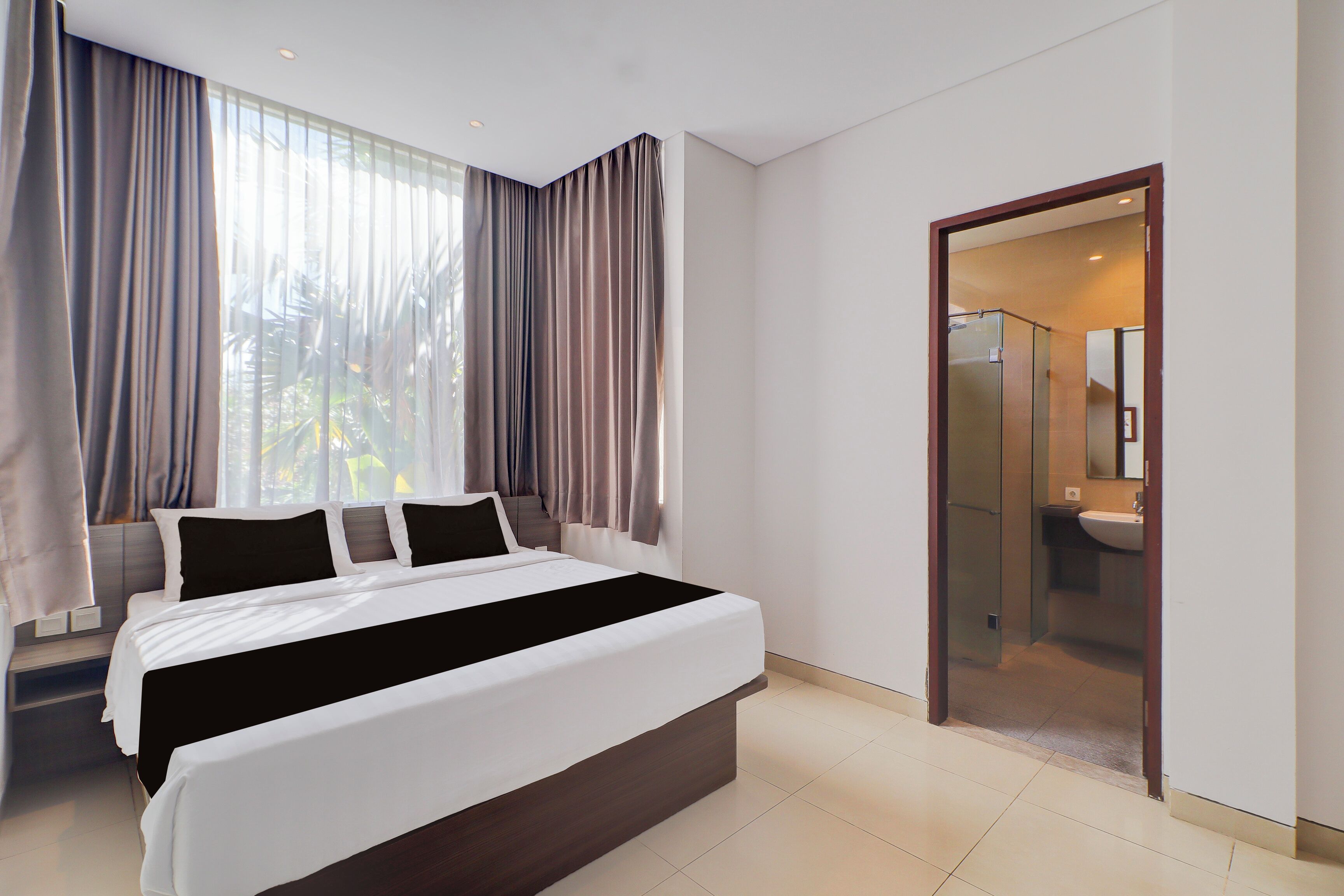 Habitación de hotel moderna con una cama grande, baño con puerta de vidrio y vista a zonas verdes.