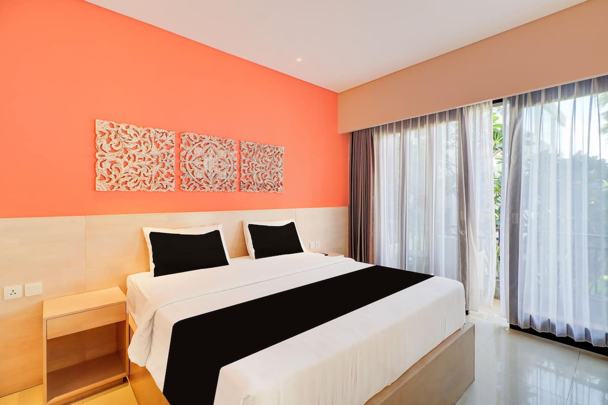 Une chambre d’hôtel moderne avec un grand lit, une table de chevet et une fenêtre ornée de rideaux légers.
