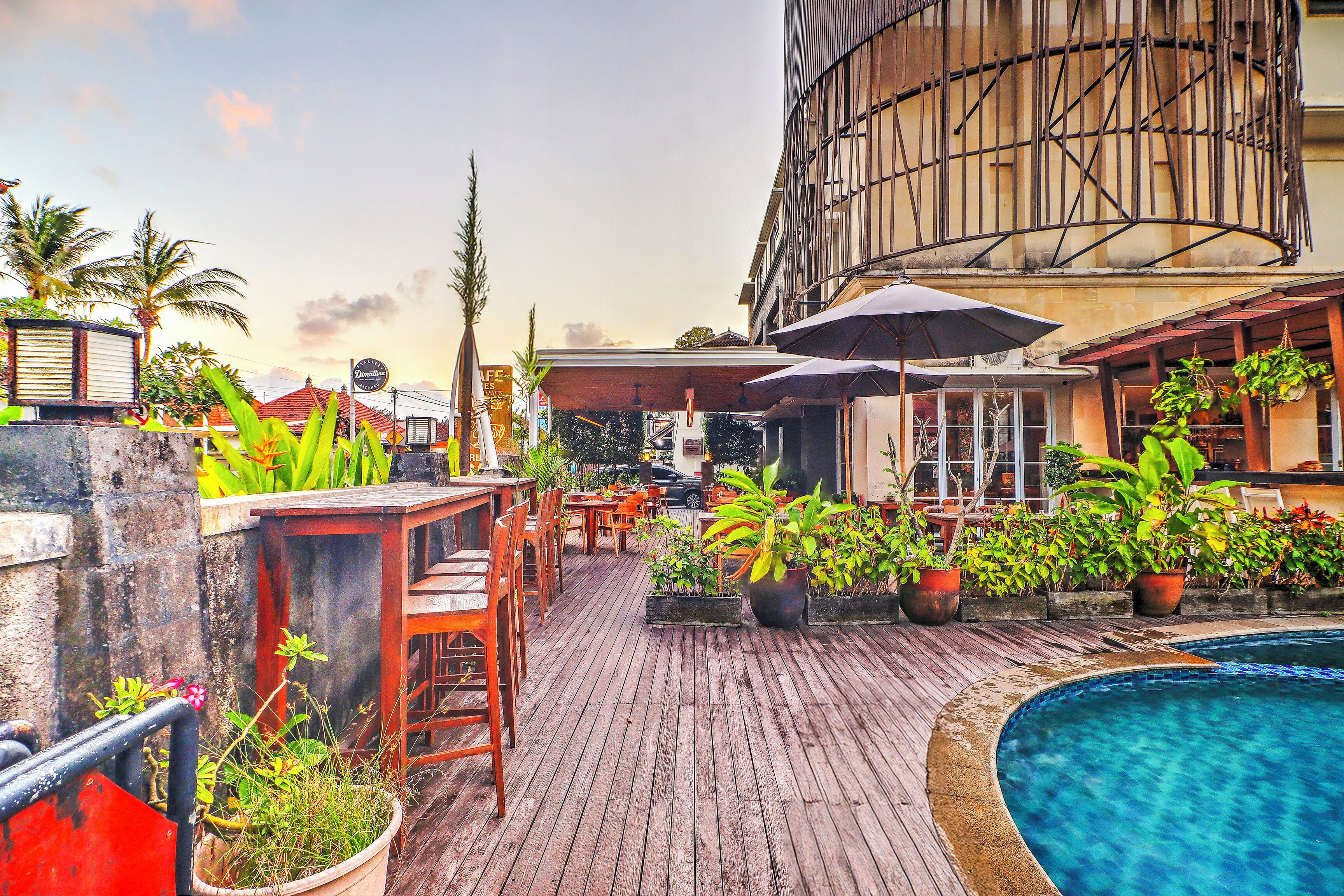 A rooftop bar with wooden flooring, potted plants, outdoor seating, and a pool.