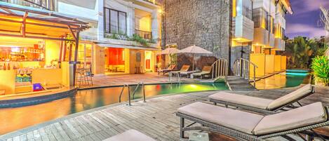 A hotel with a pool area, lounge chairs, and a bar.