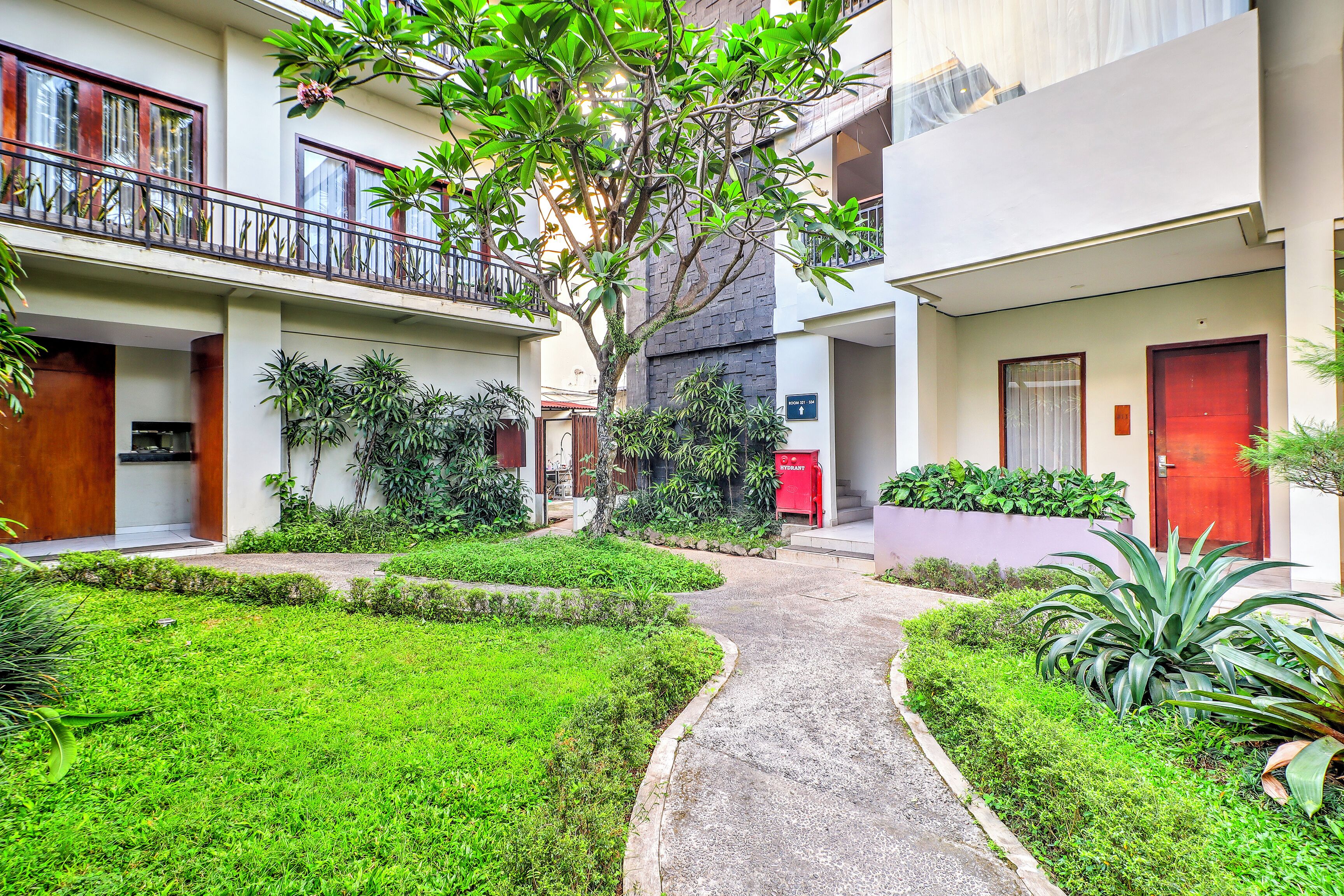 A courtyard with a central pathway, surrounded by greenery and buildings with balconies.