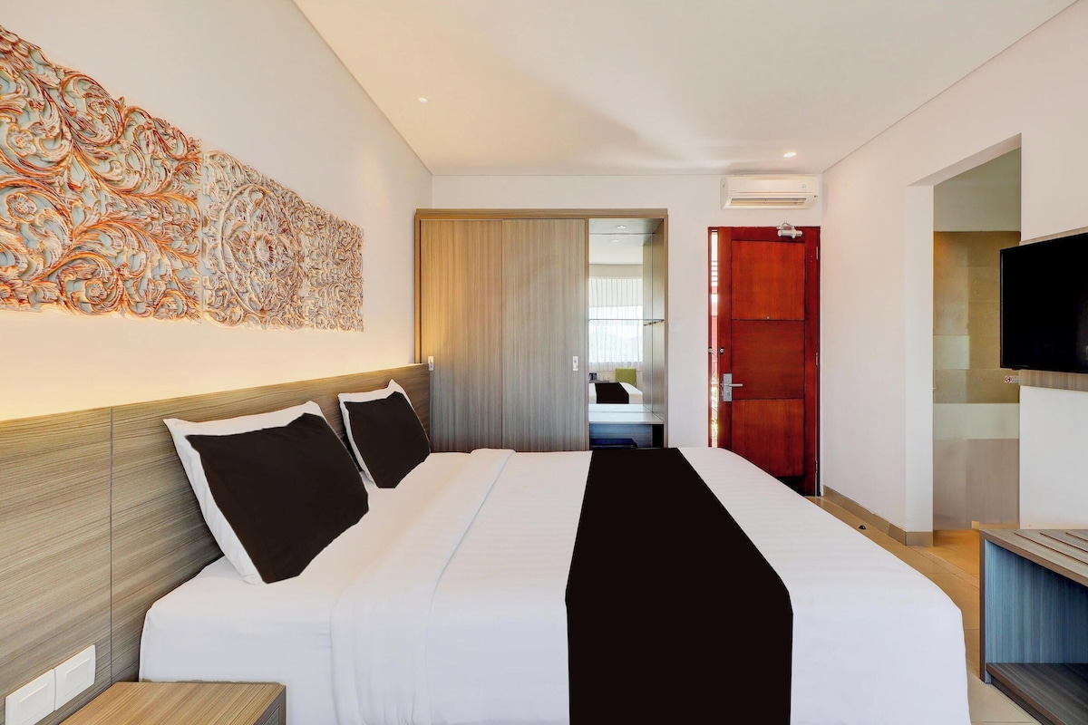 A hotel room with a large bed, a TV, and a decorative wall piece.