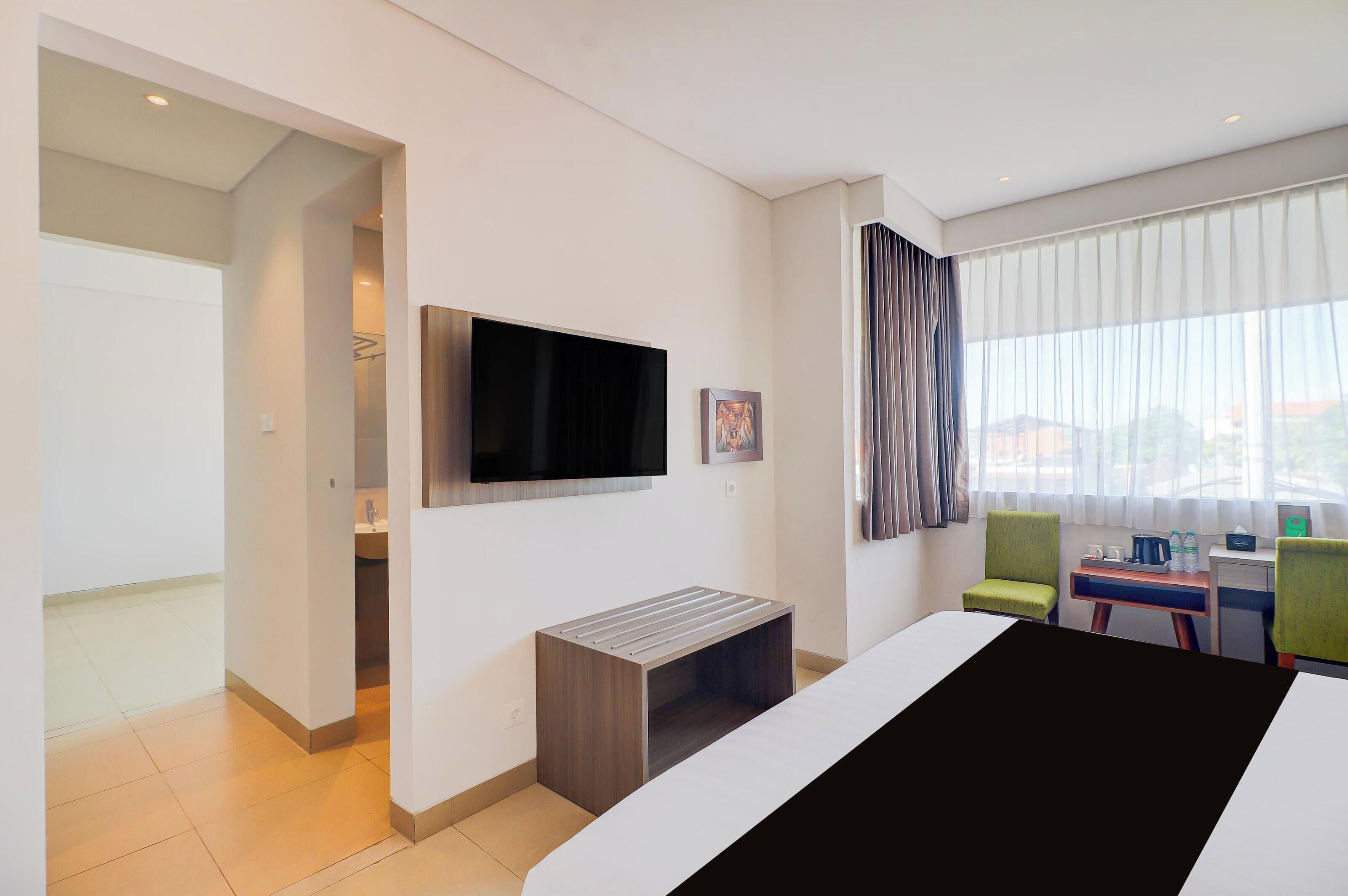 A hotel room with a bed, a TV, a desk, a chair, and a view of the city through the window.