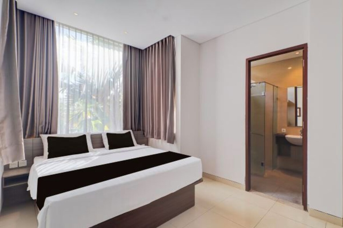 Een moderne hotelkamer met een groot bed, een inloopkast en een badkamer zichtbaar door een glazen deur.