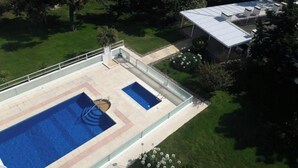 A rooftop swimming pool with a glass enclosure, surrounded by a well-maintained lawn and trees.