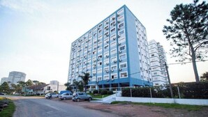 A tall, multi-story residential building with a blue and white facade, a parking area in front, and a clear sky.