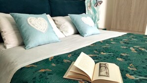 Un letto con una coperta a fiori verdi, due cuscini con motivi a cuore e un libro aperto sopra.
