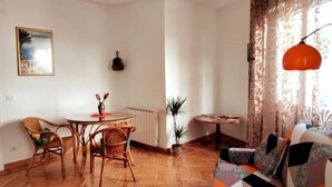 Un soggiorno con un tavolo rotondo, due poltrone in vimini, un divano, una lampada a sospensione e un quadro appeso al muro.
