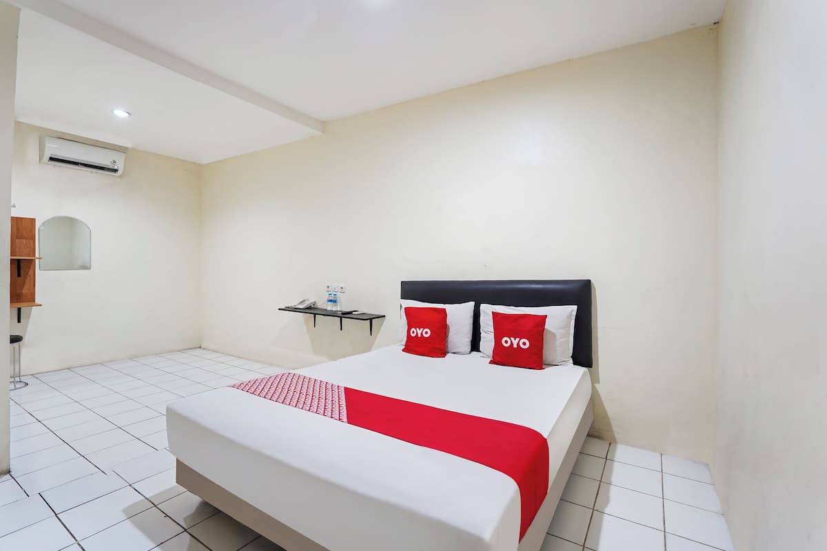 Habitación de hotel con cama, mesita de noche, aire acondicionado y una pequeña estantería con espejo y teléfono.
