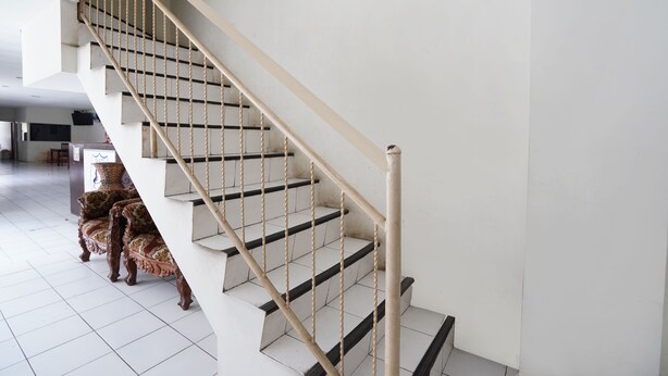 A staircase with a wooden handrail and black steps, leading to an upper floor. - OYO 91035 De Ritz Residence (Surabaya)