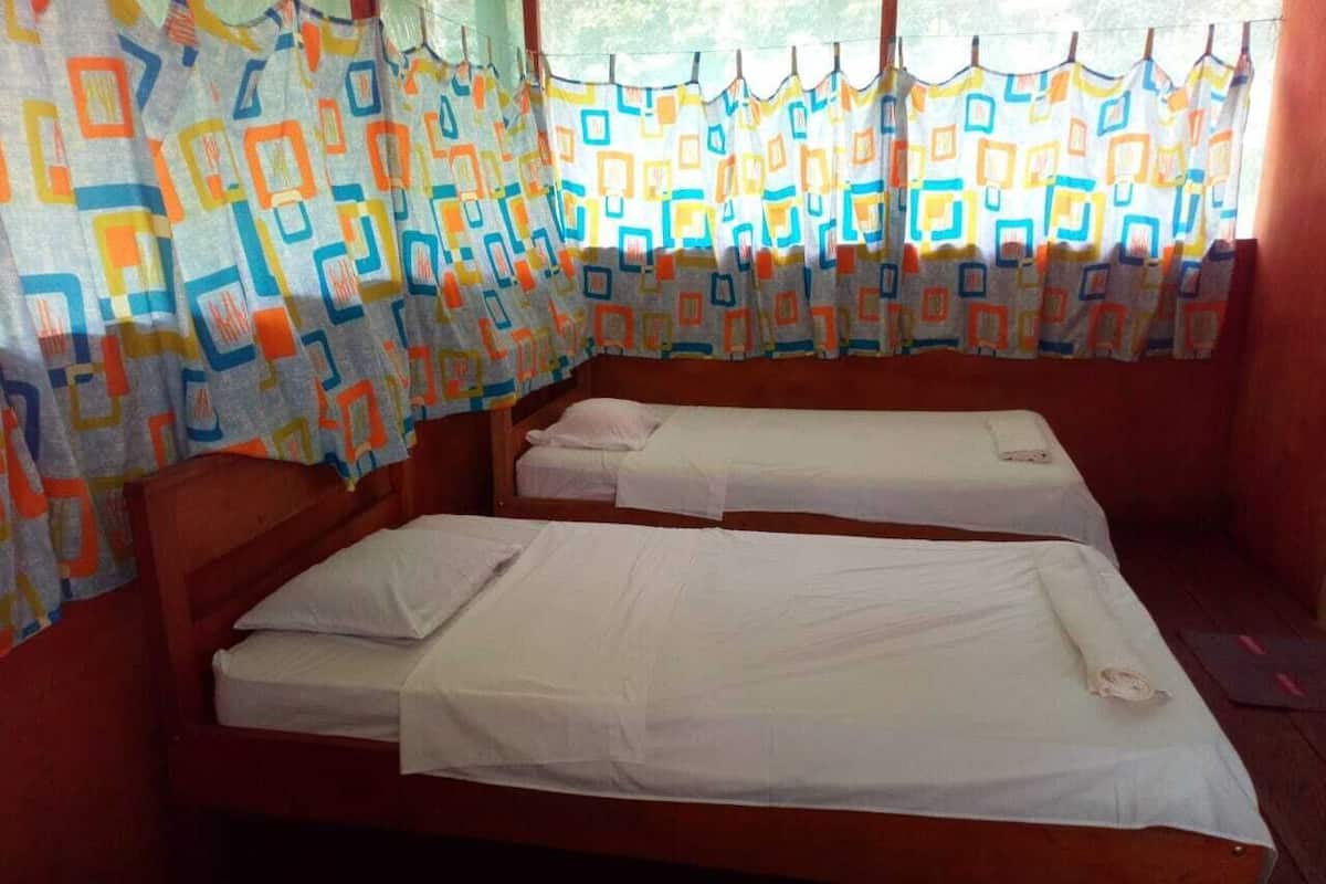 Une chambre avec deux lits simples, des têtes de lit en bois et un rideau aux motifs géométriques et aux couleurs vives.