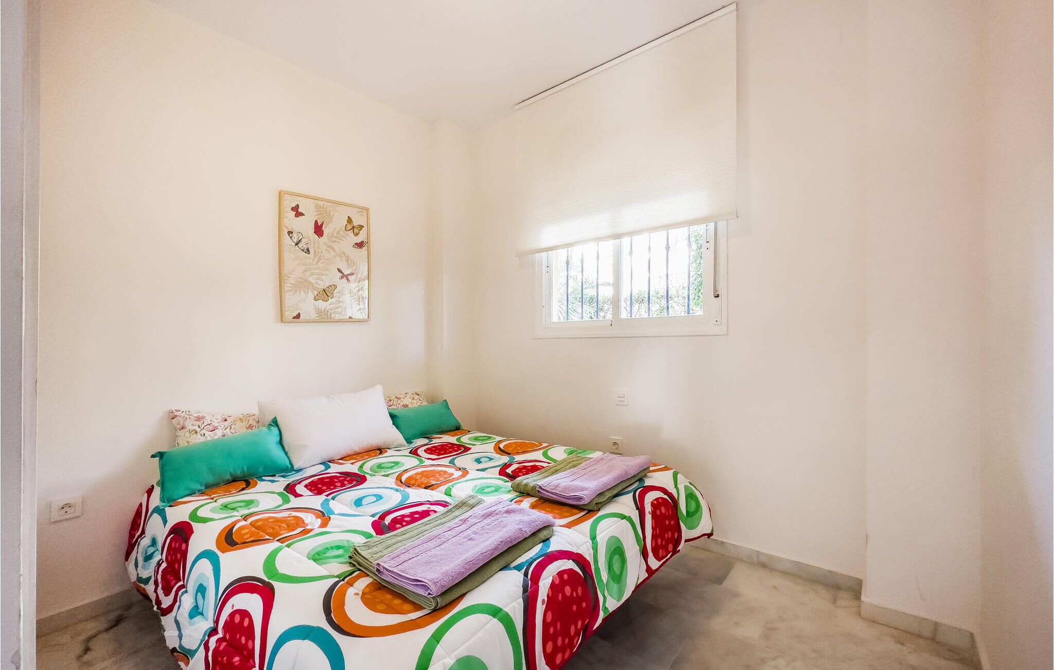A bedroom with a bed, a window, and a wall-mounted picture.