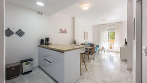 A modern kitchen with a central island, a dining area with a blue sofa, and a view of the outdoors through a large window.