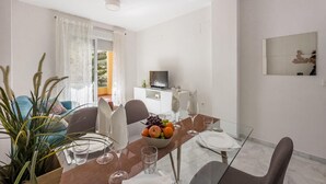 A dining area with a table set for two, a TV on a stand, and a balcony with curtains.