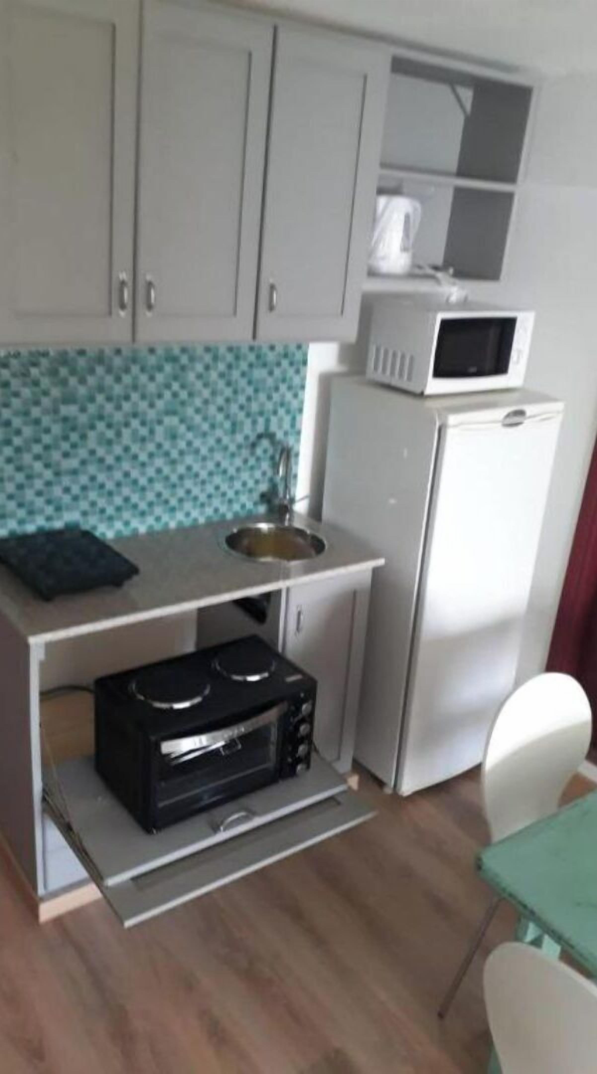 A compact kitchen with white cabinets, a microwave, a sink, and a black stove.