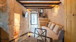 Interior con paredes de piedra, una escalera de madera, un sofá con cojines y una mesa de vidrio.