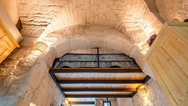 Interior con paredes de piedra, un banco de madera y una escalera que sube.