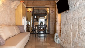 Una habitación acogedora con sofá, una mesa de comedor con sillas, televisor montado en la pared y una pared de piedra.