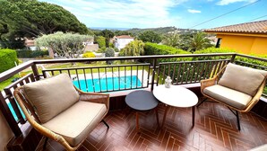 Ein Balkon mit Korbmöbeln, einem kleinen runden Tisch und Blick auf ein Schwimmbad und Grünflächen.