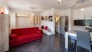A modern living space with a red sofa, a dining area, and a kitchen. - Holiday Home "Open Space Nel Sulcis" with Private Garden & A/C (Masainas)