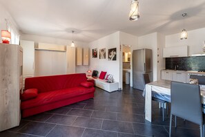 A modern living space with a red sofa, a dining area, and a kitchen.
