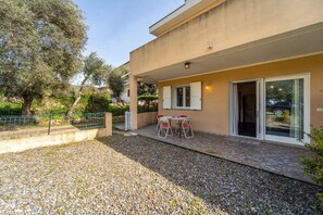 Un bâtiment doté d’un patio, d’une table avec des chaises et d’une porte donnant sur une entrée abritée.