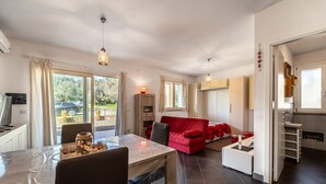 A modern kitchen with a dining area, a red sofa, and a large window. - Holiday Home "Open Space Nel Sulcis" with Private Garden & A/C (Masainas)