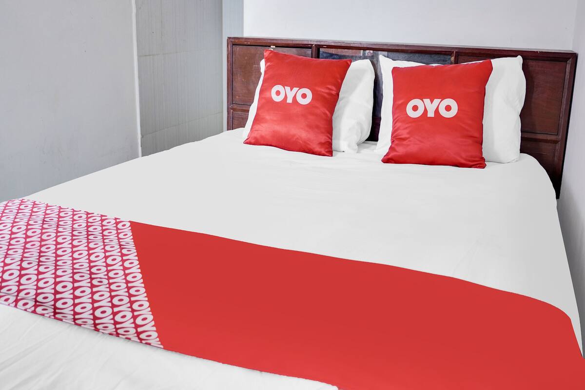 Una cama con dos almohadas rojas y una colcha blanca con estampado rojo.