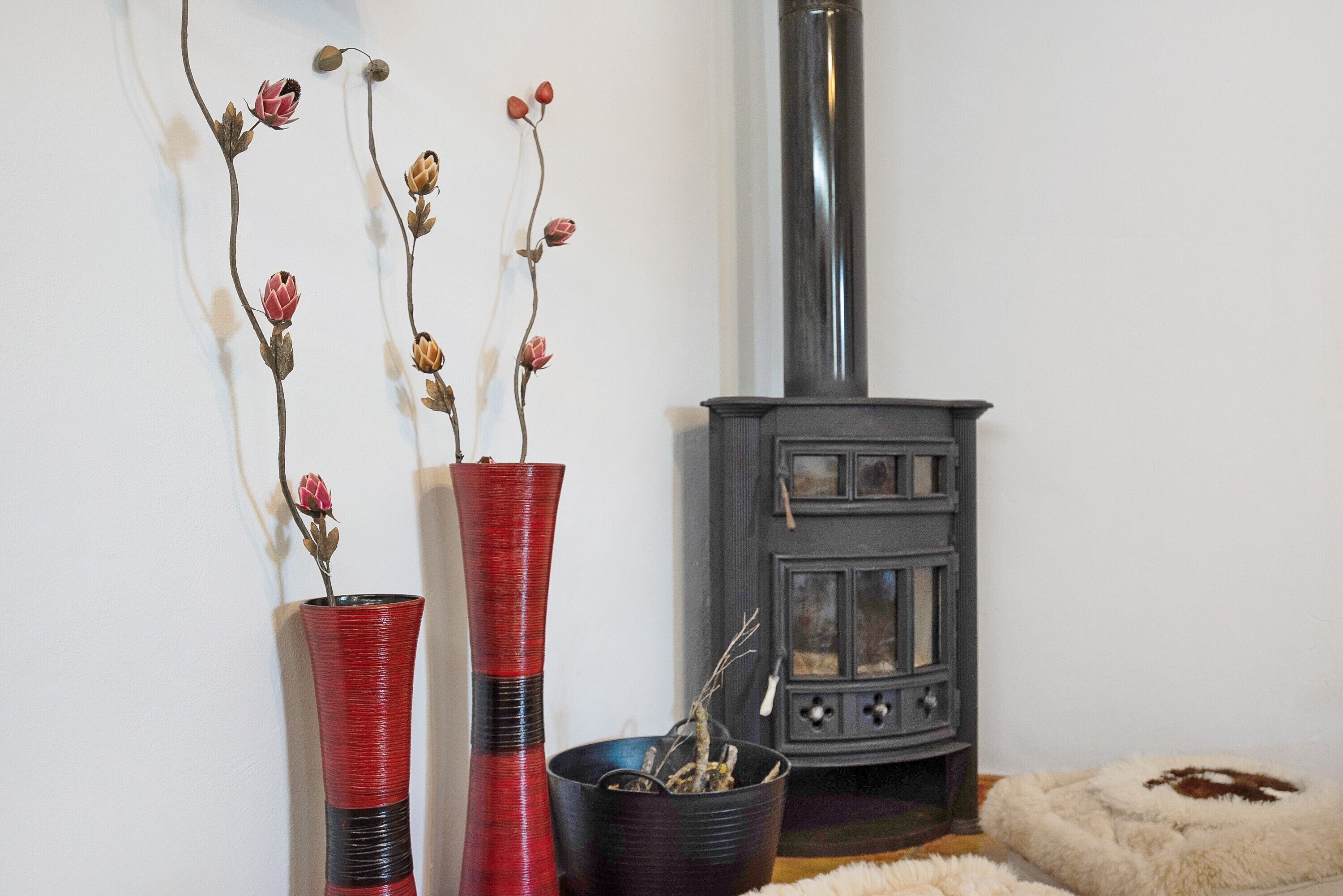 A room with a fireplace, two vases with dried flowers, and a fur rug.