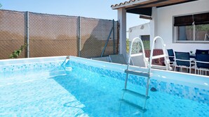 A swimming pool with a tiled edge, a ladder, and a covered seating area with chairs.