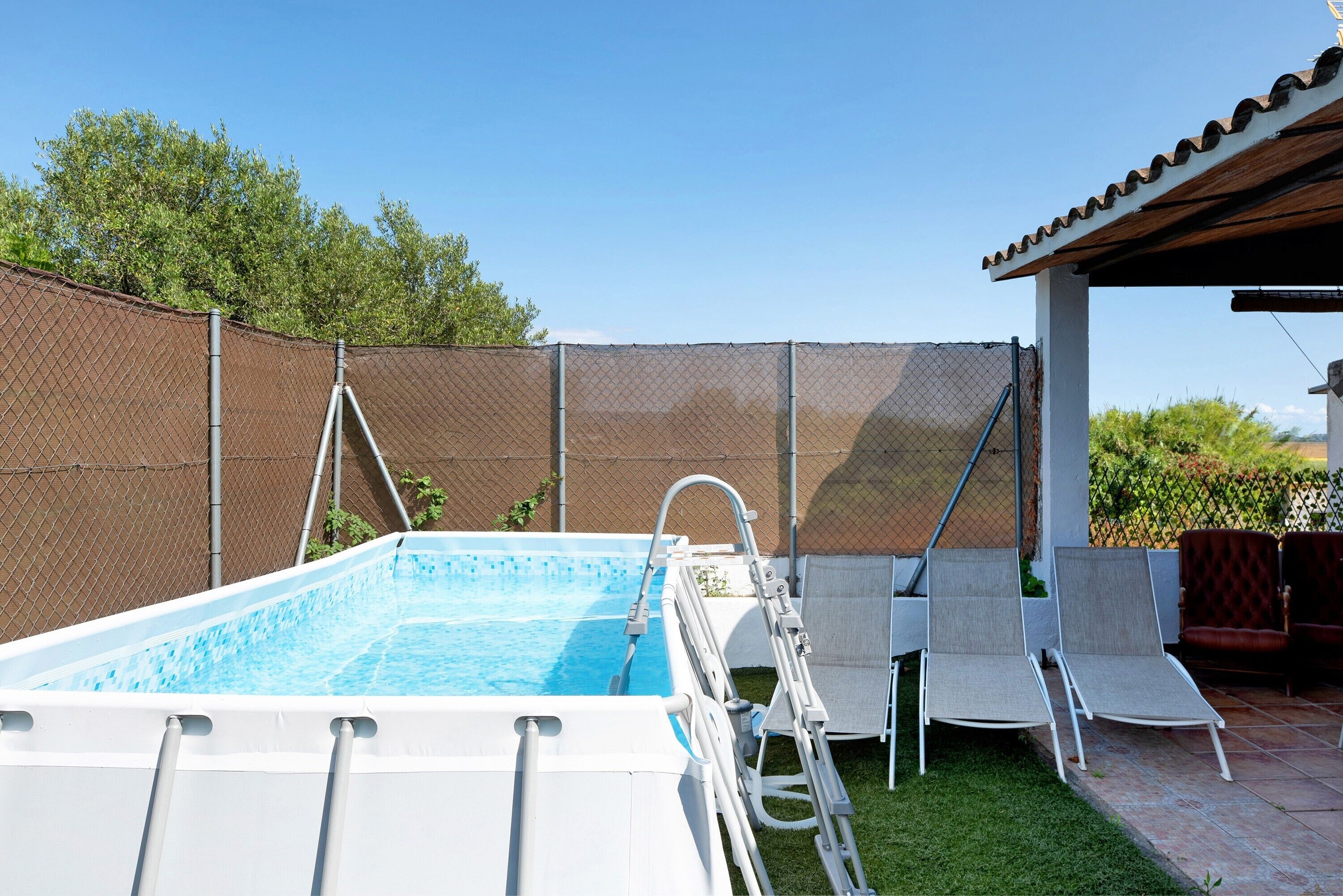 A swimming pool with a ladder, two lounge chairs, and a covered patio area.