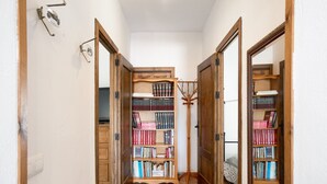 A narrow hallway with wooden doors, a bookshelf filled with books, and a wooden coat rack.